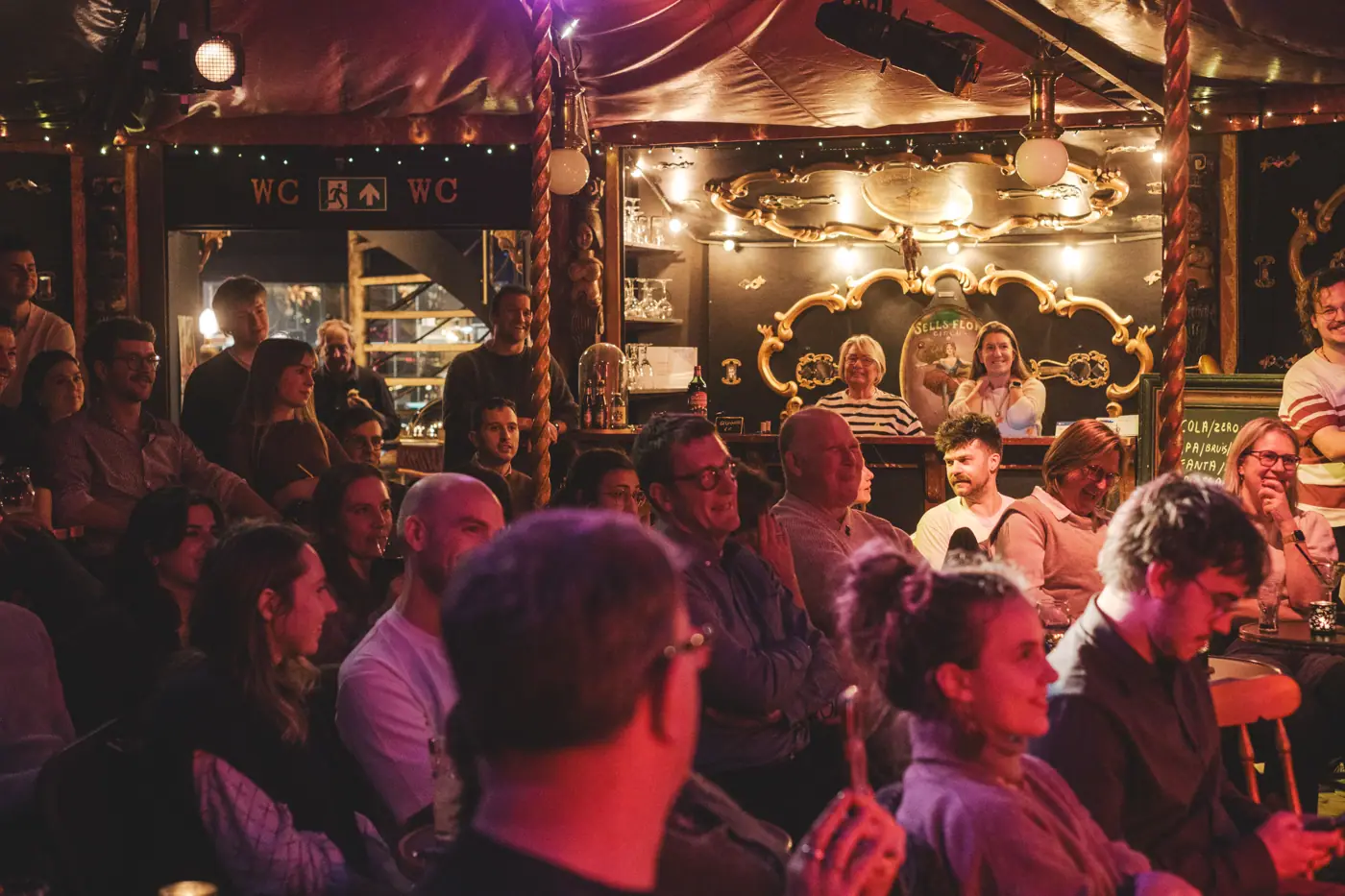 Volle zaal met warm licht en lachende gezichten aan de tafeltjes